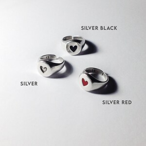 Pu&ograve; includere: Tre anelli d'argento con disegni a forma di cuore. Un anello ha un cuore nero, un altro un cuore rosso e il terzo un cuore argentato. I testi "SILVER BLACK", "SILVER" e "SILVER RED" sono visibili.