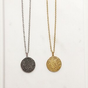 Peut inclure: Deux colliers avec des pendentifs circulaires. L'un est argent&eacute;, l'autre dor&eacute;. Les deux colliers ont une cha&icirc;ne d&eacute;licate et un pendentif rond avec un motif grav&eacute;. Les pendentifs semblent &ecirc;tre en m&eacute;tal.