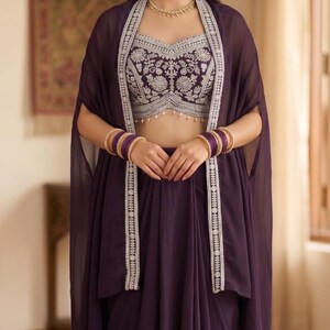 May include: A deep purple ensemble featuring a sleeveless crop top with intricate silver floral embroidery and a matching sheer cape with silver-trimmed edges. The outfit is accessorized with a gold beaded necklace and stacked purple bangles.