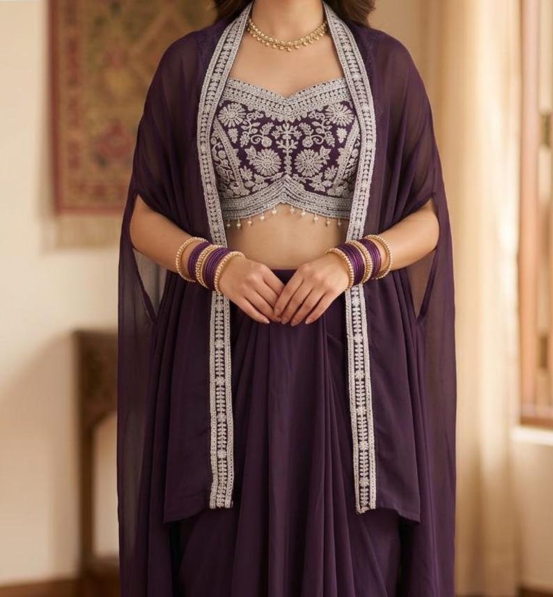 May include: A deep purple ensemble featuring a sleeveless crop top with intricate silver floral embroidery and a matching sheer cape with silver-trimmed edges. The outfit is accessorized with a gold beaded necklace and stacked purple bangles.