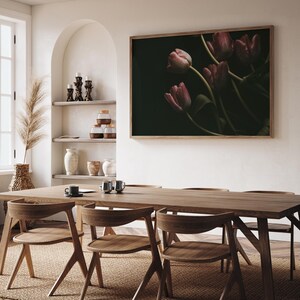 May include: A wooden dining table with four chairs, set against a white wall with a framed print of pink tulips on a dark background. The table is made of natural wood with a light brown finish. The chairs are also made of wood with a similar finish. The print is framed in a dark wood frame.