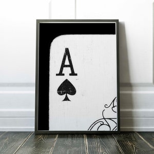 Op de afbeelding: Zwart-witte ingelijste print van een aas schoppen speelkaart met een verweerde, vintage look.