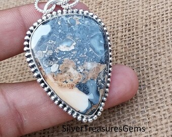 May include: A silver pendant featuring a teardrop-shaped, brown, white, and black agate stone with a beaded border. The pendant has a silver bail with a twisted design.