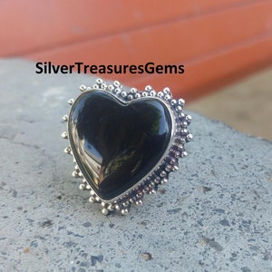 May include: A silver ring featuring a black heart-shaped gemstone. The ring has a beaded edge.