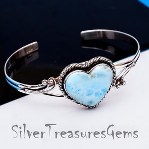 May include: A silver heart-shaped bracelet with a blue and white gemstone. The bracelet has a delicate, ornate design.