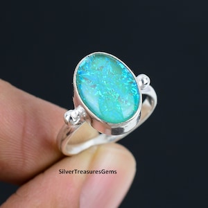 May include: A silver ring with a blue opal gemstone. The ring has a simple design with two small silver accents on either side of the stone.
