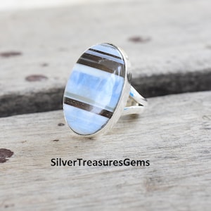 May include: A silver ring with an oval-shaped blue and brown banded gemstone.