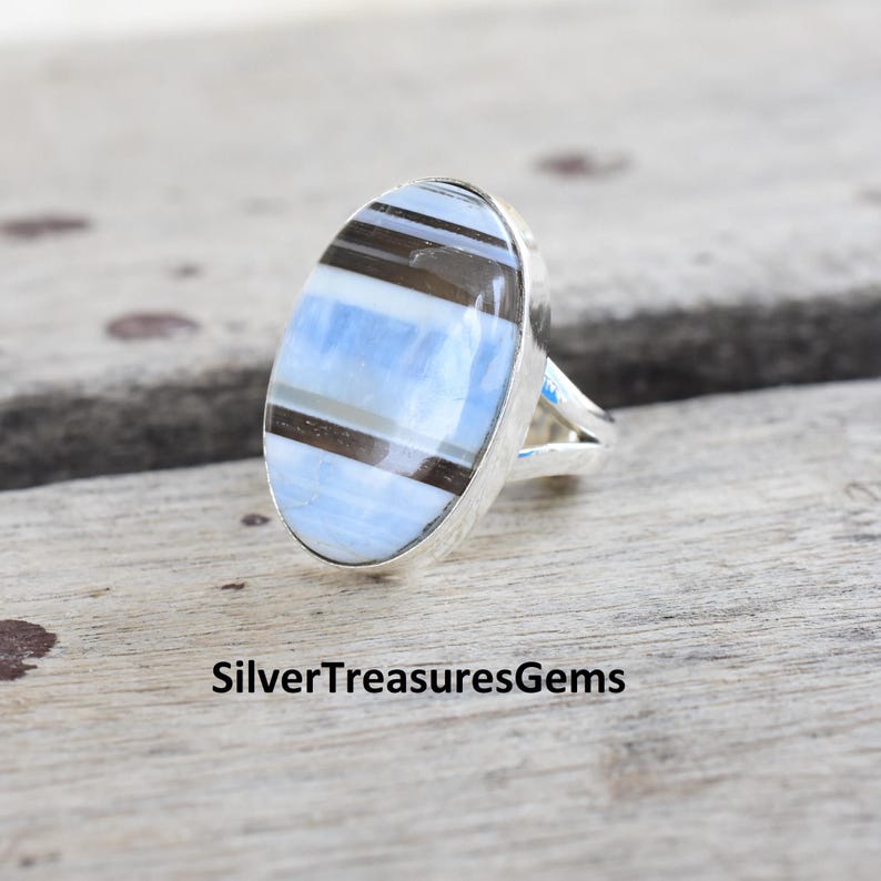 May include: A silver ring with an oval-shaped blue and brown banded gemstone.
