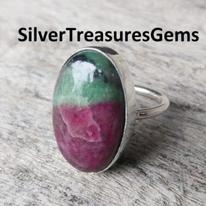 May include: Silver ring with an oval gemstone, displaying green and magenta colours. The ring has a silver band and setting. The text "SilverTreasuresGems" is displayed above the ring.
