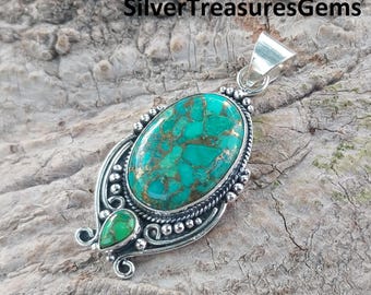 May include: A silver pendant with a large oval turquoise stone set in a silver filigree design. The stone has a green and brown marbled pattern. There is a smaller turquoise stone set in the filigree below the main stone.