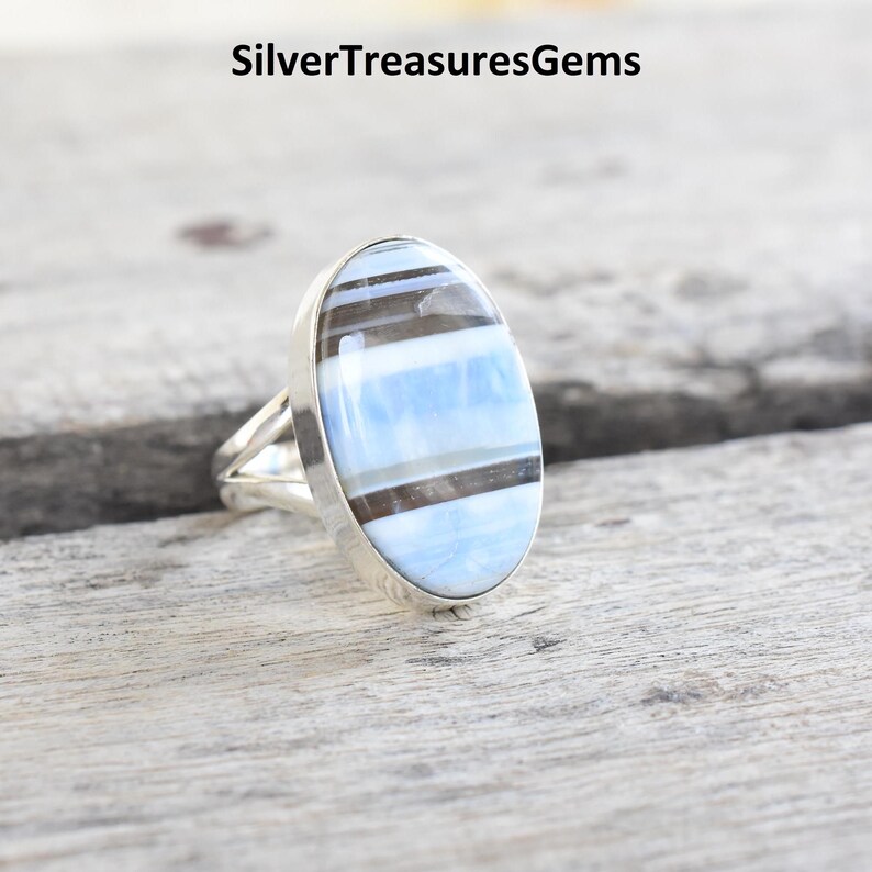 May include: A silver ring with an oval-shaped blue and black banded opal gemstone.