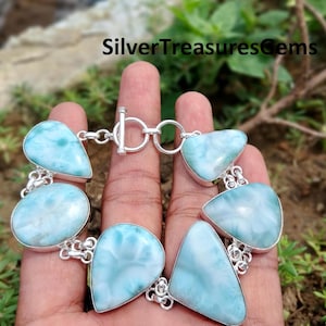 May include: A silver bracelet with a toggle clasp features a row of light blue, iridescent, teardrop-shaped stones.