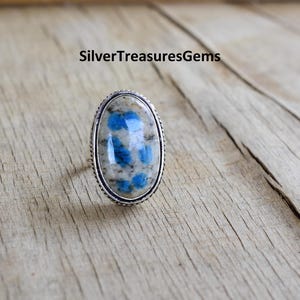 May include: A silver ring with a blue and white oval-shaped stone set in a silver bezel. The stone has a unique pattern of blue and white.