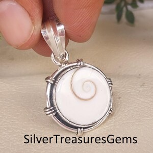 Könnte beinhalten: Silberanhänger mit weißem, spiralförmigem Mittelteil. Der Anhänger hat ein kreisförmiges Design mit einem Silberrahmen und einer Öse. Der Text "SilverTreasuresGems" befindet sich am unteren Bildrand.
