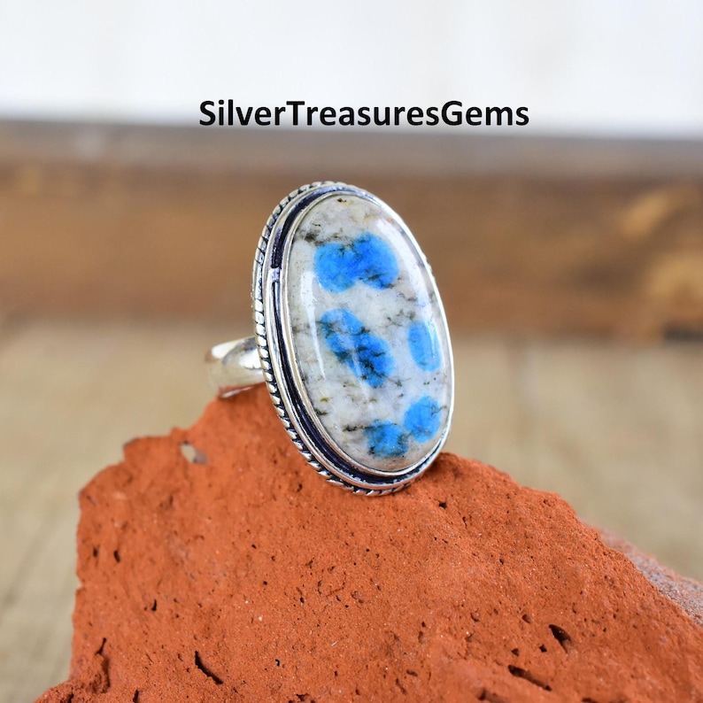 May include: A silver ring with an oval-shaped blue and white kyanite gemstone. The ring is set in a silver band with a decorative border.