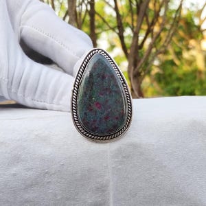 Puede incluir: Un anillo de plata con una piedra preciosa verde y roja en forma de lágrima engastada en un engaste de plata.