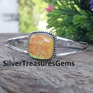 Op de afbeelding: Zilveren manchetarmband met een vierkante, iriserende oranje edelsteen. De edelsteen is gezet in een zilveren kralenframe. De armband heeft een gespleten bandontwerp. De tekst "SilverTreasuresGems" staat onderaan.