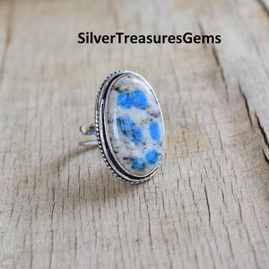 May include: A silver ring with a blue and white oval gemstone. The gemstone has a unique pattern of blue spots on a white background.