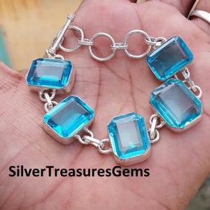 May include: A silver bracelet with a chain link design and five blue gemstone rectangular links. The bracelet has a toggle clasp.