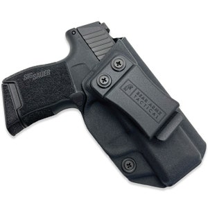 May include: A black Sig Sauer handgun in a black Bear Armz Tactical holster. The handgun is partially visible, with the textured grip and the "SIG Sauer" logo clearly displayed. The holster features a belt clip and is secured with screws.