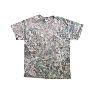 May include: A short-sleeved camouflage t-shirt with a crew neck. The shirt features a pattern of green, brown, and tan leaf-like shapes, creating a woodland camouflage design. The shirt is made of a lightweight material.