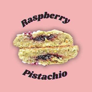 May include: A cross-section of a raspberry pistachio cookie, revealing a dark jam filling and pistachio-flecked dough. The cookie is cut in half, showcasing the texture. The words "Raspberry" and "Pistachio" are arched above and below the cookie on a pink background.
