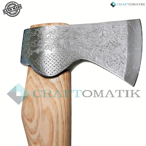 May include: A hand-forged axe with a wooden handle and a detailed floral design etched into the metal head. The axe is labelled "CRAFT OMATIK" and "HAND MADE ORIGINAL".