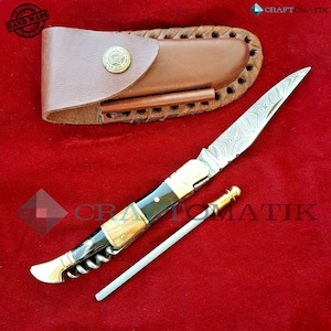 May include: A pocket knife with a wood and black handle, a corkscrew, and a metal rod. The knife has a patterned blade and comes with a brown leather sheath.
