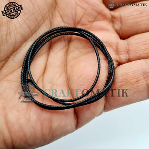 May include: Black waxed cord, approximately 1.5 mm thick, wound in a coil on a hand. The cord is made for jewellery making and crafting.