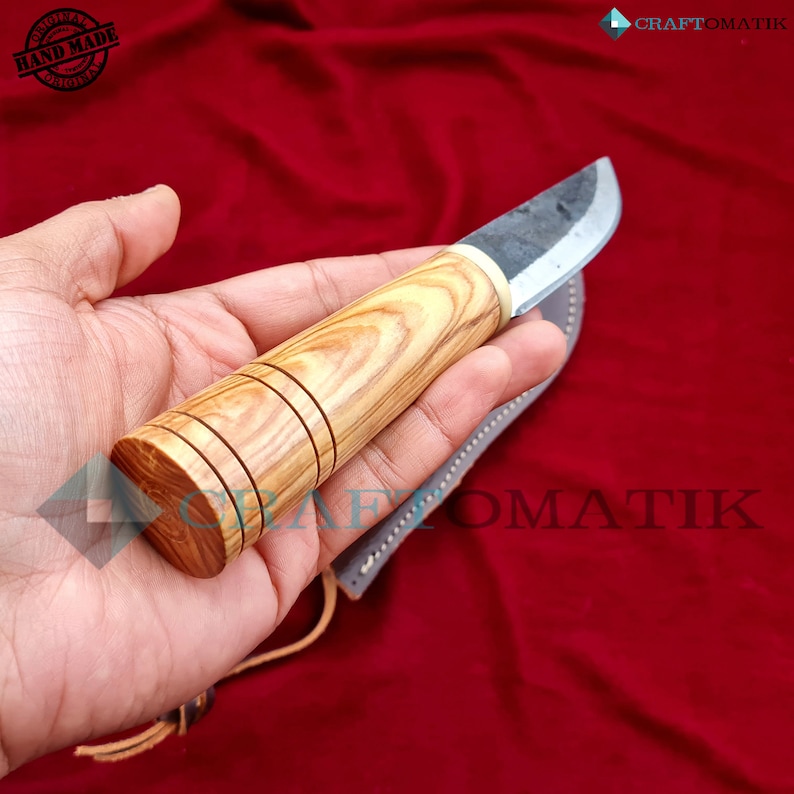 May include: A handmade knife with a wooden handle and a leather sheath. The handle is made of olive wood and has a dark brown stain. The blade is made of steel and has a slight curve. The knife is approximately 8 inches long.