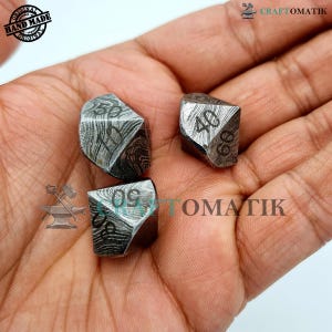 Puede incluir: Tres dados de metal con un diseño único y estampado. Cada dado tiene un número diferente en cada lado, con los números 30, 40 y 60 visibles en la imagen.