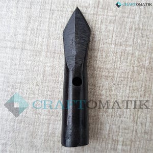 Könnte beinhalten: Ein schwarzer Metallpfeilspitz mit einer spitzen Spitze und einem Loch in der Mitte. Der Pfeilspitz ist etwa 15 cm lang.