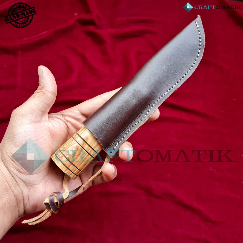 May include: A brown leather knife sheath with a wooden handle. The sheath has stitching around the edges and a leather strap. The handle is made of wood with a striped pattern. The knife is handmade and original.