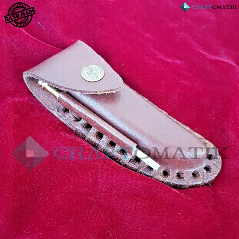 May include: A brown leather sheath with a decorative stitching pattern and a brass button. A small, silver-colored knife is inside the sheath.
