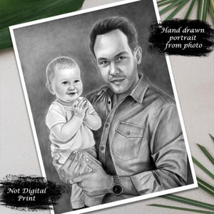 May include: A black and white pencil drawing of a father holding his young son. The father is wearing a button-down shirt and the son is wearing a white shirt. The drawing is labelled "Hand drawn portrait from photo" and "Not Digital Print".