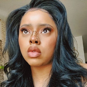 May include: A woman with long, dark, wavy hair wearing a black strapless top. She is wearing a gold nose ring.