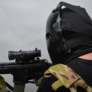 May include: A person wearing a black tactical helmet and a camouflage vest holds a black rifle with a scope.
