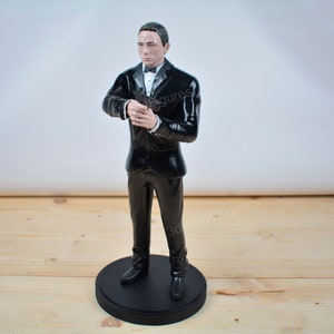 Pu&ograve; includere: Statuetta di un uomo in smoking nero, camicia bianca e papillon nero. La figura &egrave; in piedi su una base circolare nera. L'uomo tiene le mani giunte davanti a s&eacute;. La statuetta &egrave; un oggetto da collezione.