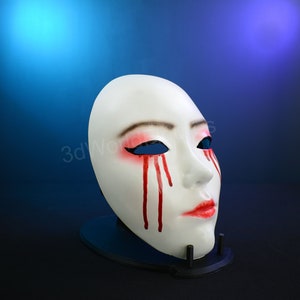 May include: White plastic mask with red painted blood dripping from the eyes. The mask has a feminine face with closed lips and black painted eyes.