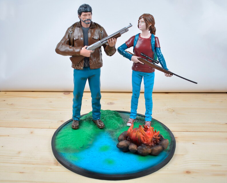Pu&ograve; includere: Un set di figurine dettagliate raffiguranti due personaggi, uno con un fucile a canna liscia e l'altro con un fucile. Si trovano su una base circolare con un paesaggio dipinto, tra cui un fal&ograve; e acqua. Le figure sono vestite in modo casual.