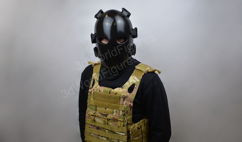 May include: A person wearing a black tactical helmet with a face shield and a camouflage tactical vest.