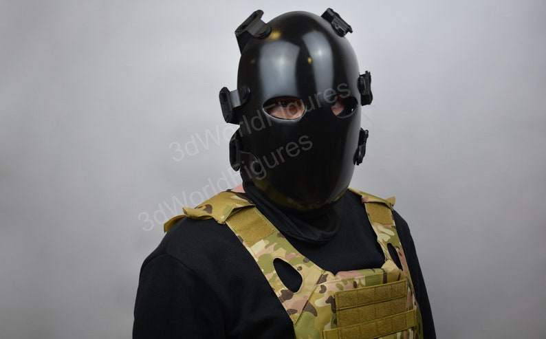 May include: A black tactical helmet with a face shield and straps. The helmet is worn by a person wearing a black shirt and a camouflage vest.