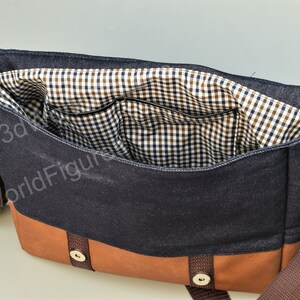 May include: A blue denim messenger bag with a brown leather bottom and a brown strap. The bag has a checkered fabric lining and a small pocket inside.