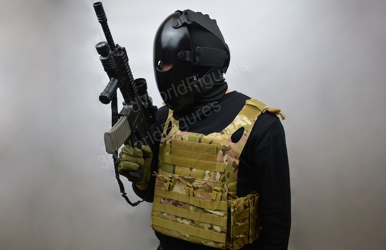 May include: A person wearing a black tactical helmet and a black balaclava holds a black rifle with a scope. The person is wearing a tan tactical vest with multiple pouches.