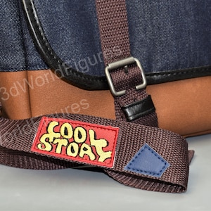 May include: A brown and dark blue messenger bag with a brown adjustable strap. The strap has a red patch with the words "Cool Story" in yellow lettering.