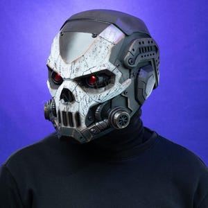 Può includere: Un casco tattico integrale caratterizzato da una piastra frontale bianca invecchiata a forma di teschio con segni neri usurati. Il casco include pannelli laterali grigio scuro, prese d'aria circolari e lenti oculari rosse luminose.