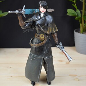 Pu&ograve; includere: Statuetta dettagliata di un personaggio in un cappotto nero con mantello, che tiene una spada e una pistola. La figura ha guanti marroni e una cintura. La spada ha un'impugnatura avvolta in blu. Oggetto da collezione.