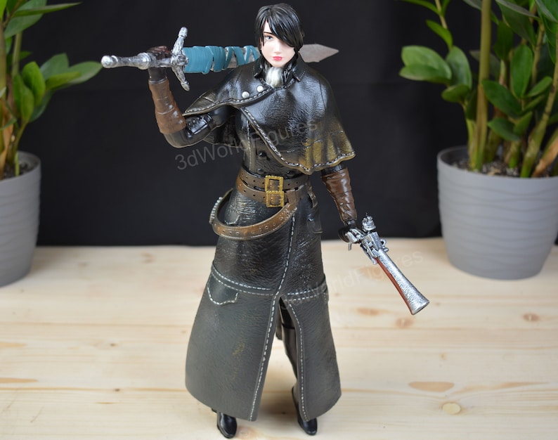 Pu&ograve; includere: Statuetta dettagliata di un personaggio in un cappotto nero con mantello, che tiene una spada e una pistola. La figura ha guanti marroni e una cintura. La spada ha un'impugnatura avvolta in blu. Oggetto da collezione.