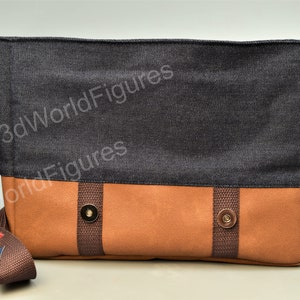 May include: A brown and black canvas messenger bag with a brown strap and a gold button closure. The bag has the text "3dWorldFigures" printed on it.