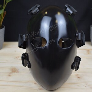 May include: A black protective face mask with adjustable straps. The mask has two eye holes and a smooth, glossy finish.